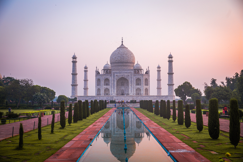 The Taj Mahal during sunrise. This is one of the most famous landmarks in Asia. It shows the front of the Taj Mahal and the sky is pink and yellow.